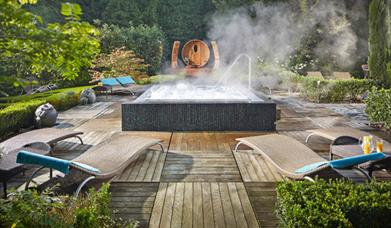 outdoor decking with chaise long chairs around a large hot tub with greenery and plants all around