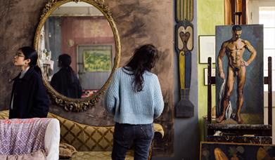 Charleston, Firle, the studio, two visitors, painting of naked man on easel and another painting lying on the floor, two sofas and large mirror on the