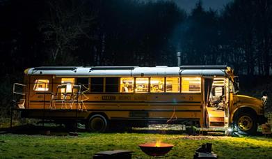 night time image of US school bus conversion in a field with a fire pit