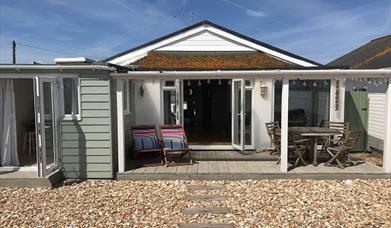The outside of the Driftwood Beach House with the doors and deckchairs leading directly onto the pebble beach