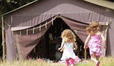 Two young girls running into yurt at Canfield Farm