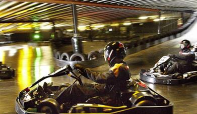 Go karts going around a track - action shot - people in the go karts wearing protective clothing and helmets
