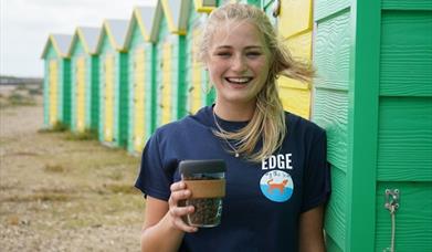 Smiling staff member from Edge by the Sea independent coffee shop infront of green and yellow beach huts in Littlehampton, Sussex|A selection of homem