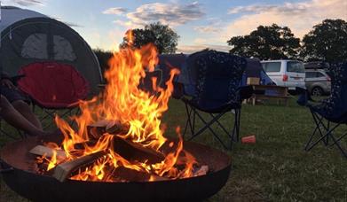an early evening fire pit with flames and camping chairs around it