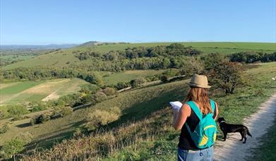 scenic view of the downs with a woman studying a map and a dog by her side