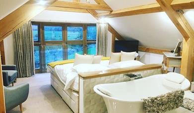 Large guest room with wooden beams and bath tub behind bed