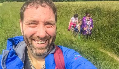 man doing a selfie - walking on a trail with family in the background