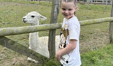 girl smiling next to a llama in a pen