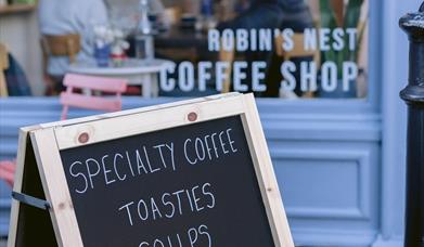 A sandwich board outside Robin's Nest Coffee Shop reads "Specialty coffee, toasties, soups, homemade cakes. Open 7.30 - 4 Monday to Friday, 10 - 4 Sat