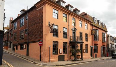 Exterior of The George In Rye, wrought iron balcony above entrance columns, and side hanging signs.