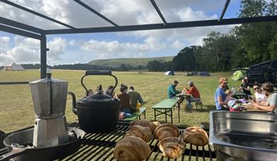 coffee pot and croissants at the outdoor kitchen with people sitting in the background