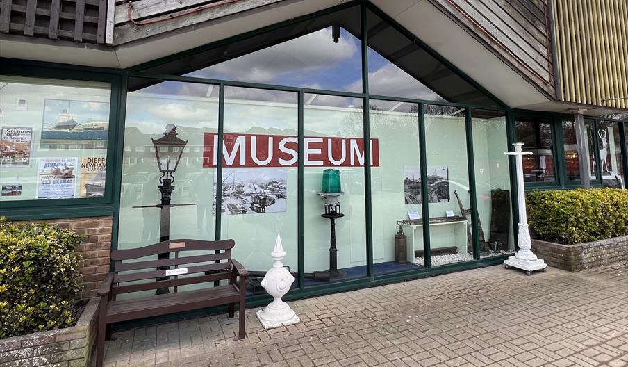 Outside a glass fronted image of Newhaven Museum showing images and objects against a pale green background
