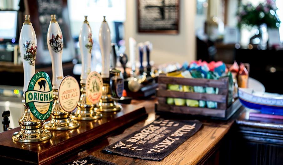 4 traditional pull style beer pumps showing real ales on a wooden pub bar with beer mats at The Cat Inn