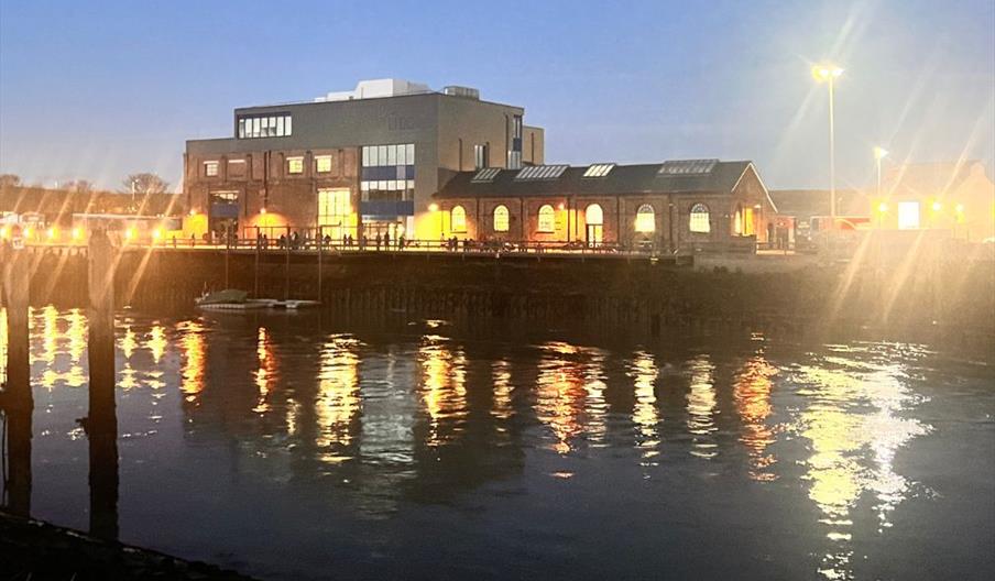 The Marine Workshops venue on Newhaven's riverside, lit up at night and reflected in the river.