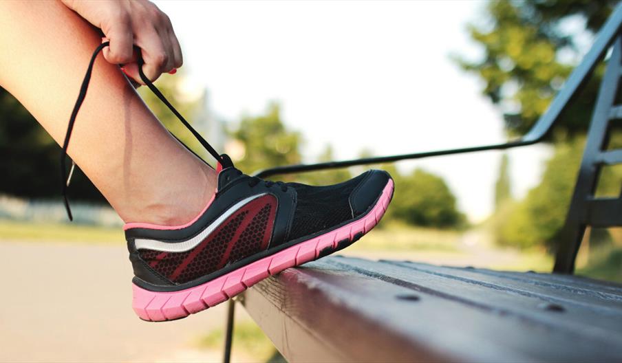 Person tying their laces on a wooden bench
