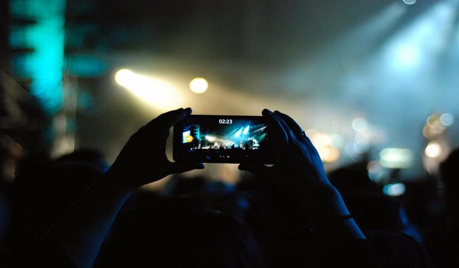 Hands holding a mobile phone taking a picture at a concert