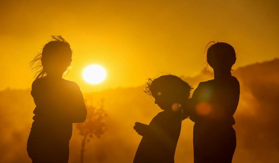 Three children silhouetted against a vibrant sunset