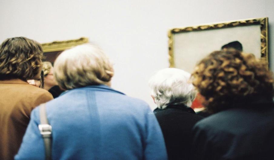 View of backs of four adults viewing paintings in an art gallery