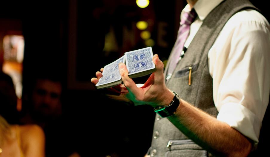 Person with grey waistcoat holding a deck of cards