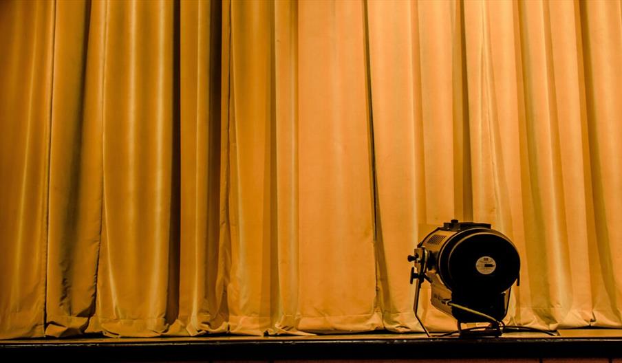 Dark yellow velvet stage curtain with spotlight in foreground