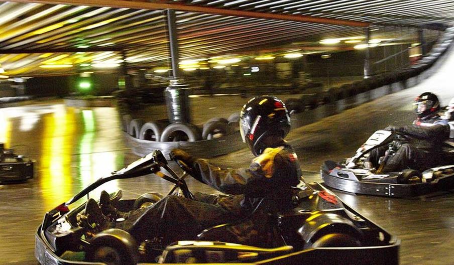 Go karts going around a track - action shot - people in the go karts wearing protective clothing and helmets