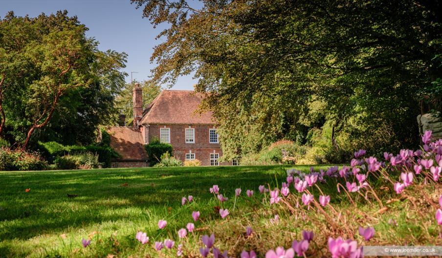 Farleys House & Garden with overhanging trees, grass lawn and pink flowers in the foreground