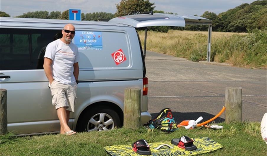 instructor standing by his van with a kiteboard on the grass