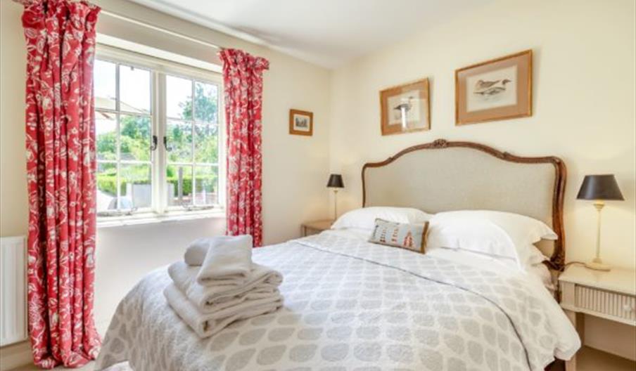 A room with a double bed, with towels placed at the end of it. 3 small paintings of ducks around the room. A window looking out onto the garden, with