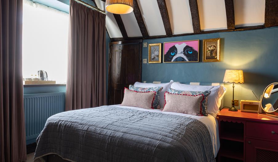 A cosy bedroom with double bed and quirky art work. exposed beams on ceiling and warm lighting