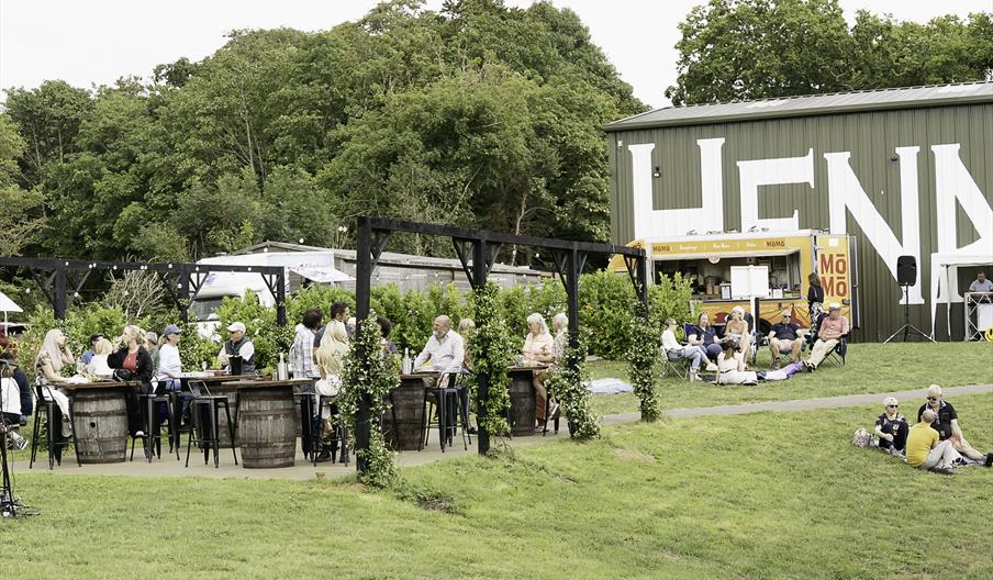 Out door seating with people sitting at tables and on the grass in front of the winery building