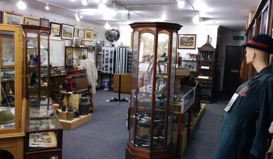 The interior of Henfield Museum with wooden display cabinets, paintings and a costume manikin.