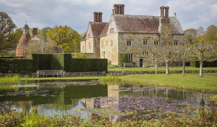 National Trust Bateman's House, pond in the foreground, surrounded by a bench, hedge and trees