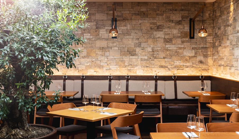 Inside the restaurant with wooden tables in the centre and cushioned bench seating along the walls.
