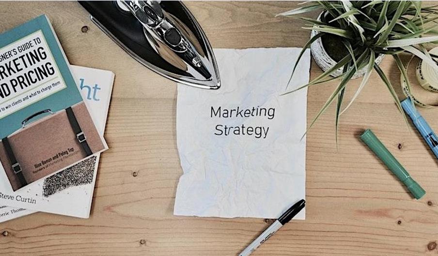 image of a desk with a crumpled sheet of paper saying marketing strategy and an iron about to straighten the crumple lines
