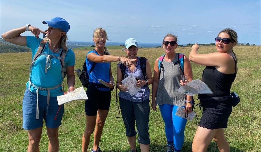 A group of ladies in the countryside holding maps smiling and wondering which direction to travel.