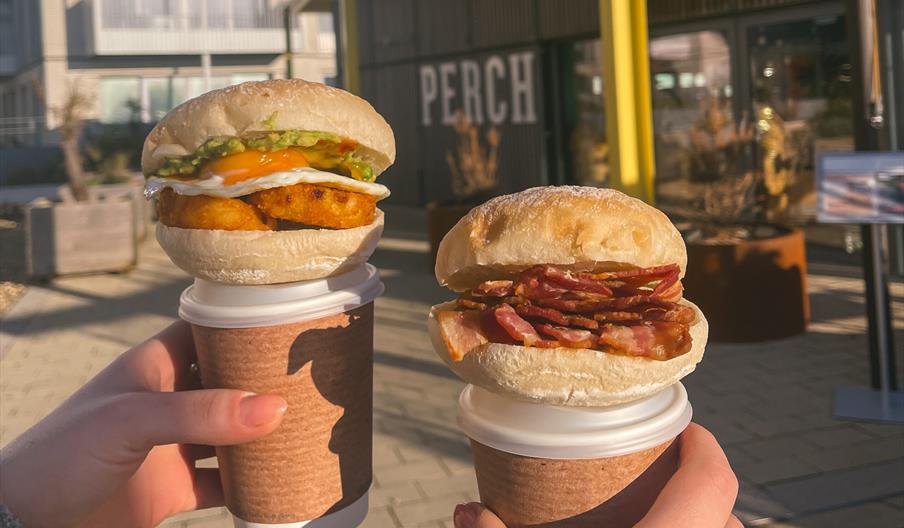 Two hands holding breakfast buns and coffees in from of the venue