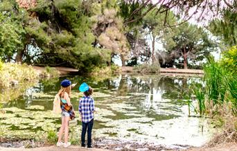 Two kids at the side of a lake in a garden