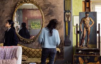 Charleston, Firle, the studio, two visitors, painting of naked man on easel and another painting lying on the floor, two sofas and large mirror on the