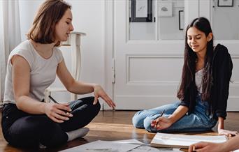 Two people sat on the floor between art supplies