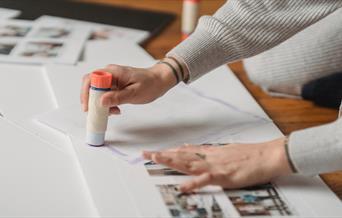 A person with tattoos using a glue stick on paper