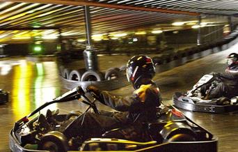 Go karts going around a track - action shot - people in the go karts wearing protective clothing and helmets
