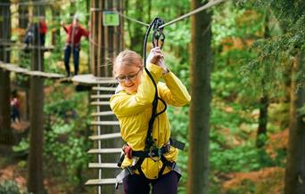 Children climbing on Go Ape treetop course holding on to ropes