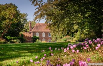 Farleys House & Garden with overhanging trees, grass lawn and pink flowers in the foreground