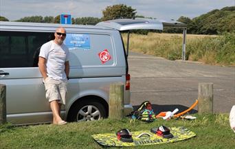 instructor standing by his van with a kiteboard on the grass