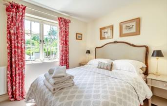 A room with a double bed, with towels placed at the end of it. 3 small paintings of ducks around the room. A window looking out onto the garden, with