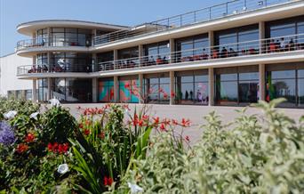 De La Warr Pavilion, Bexhill On Sea exterior, flowers in the foreground, visitors sitting on the outside balconies, the art exhibition and spiral stai