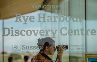 view of the window into the discovery centre with a bird watcher using binoculars