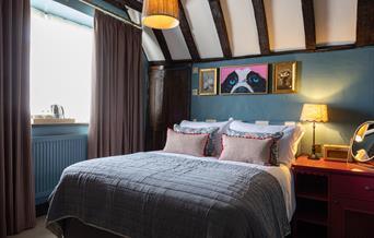 A cosy bedroom with double bed and quirky art work. exposed beams on ceiling and warm lighting
