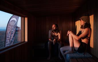 two people gazing out of the window from inside a wooden sauna