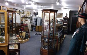 The interior of Henfield Museum with wooden display cabinets, paintings and a costume manikin.